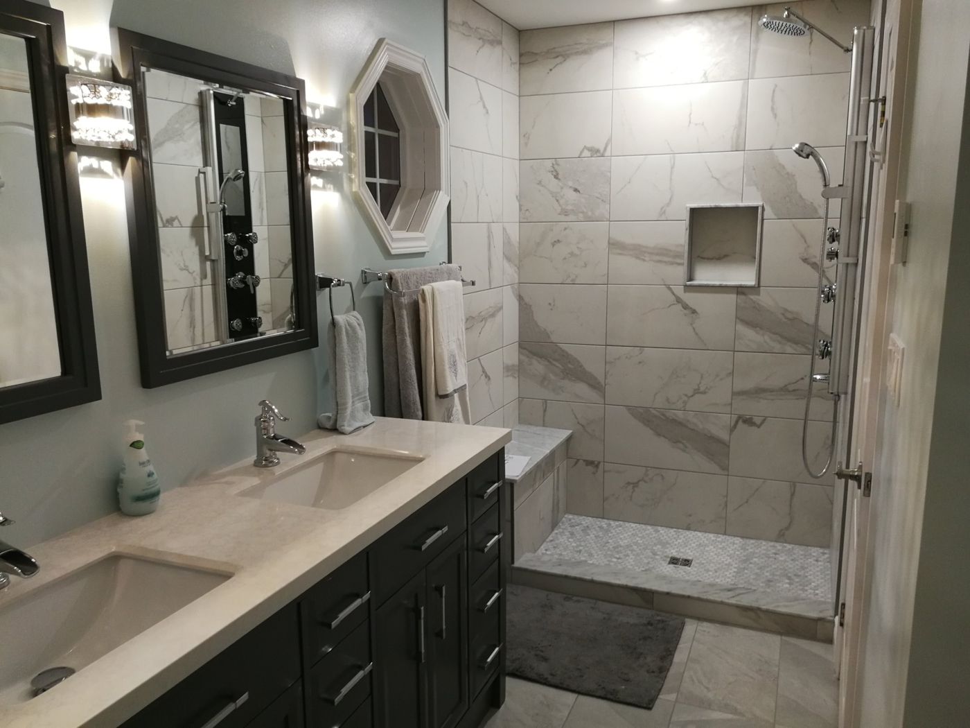 Renovated bathroom with a dark double vanity and a marble look tiled shower