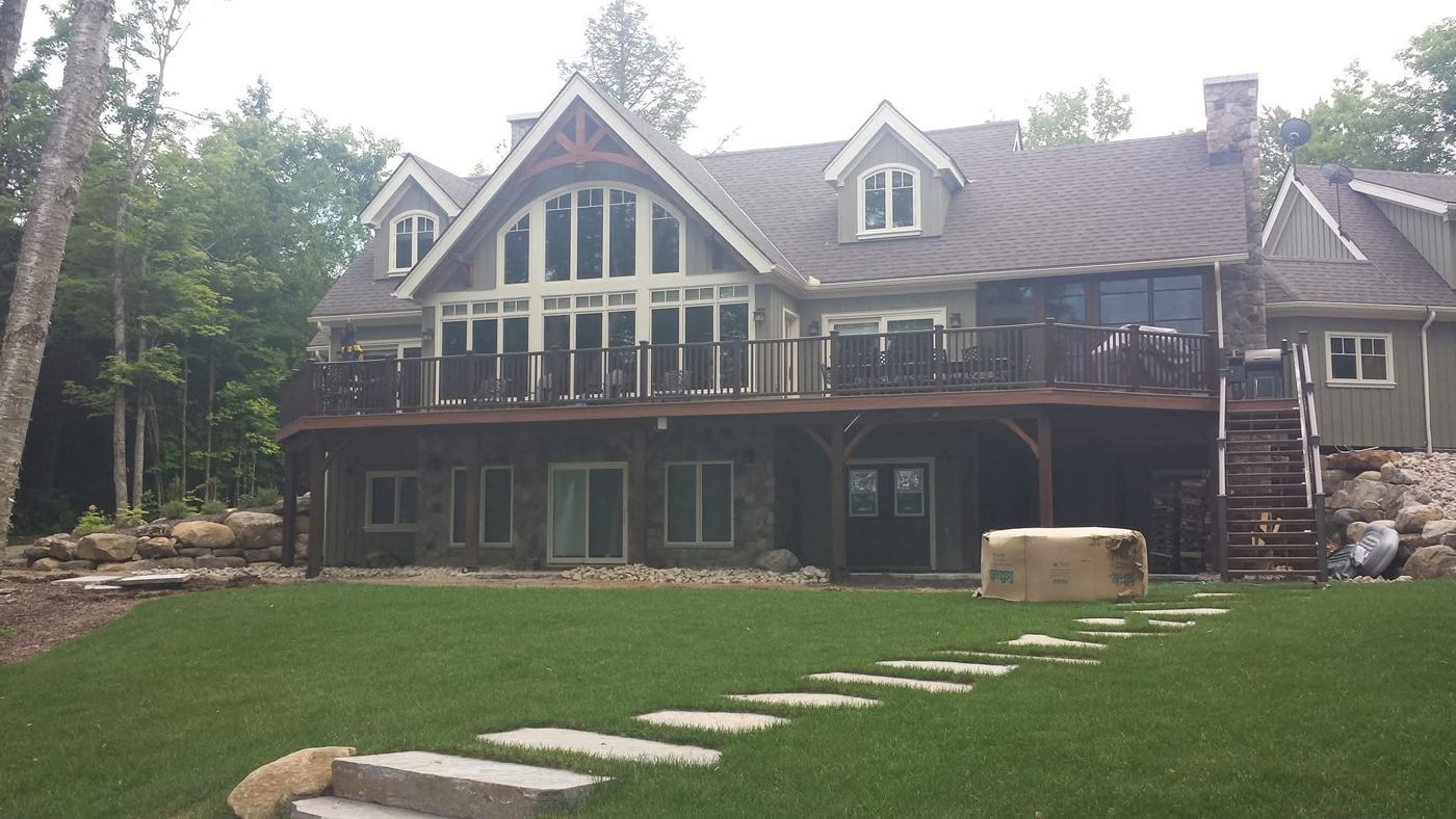 Lake house with a timber truss gable, wraparound deck and stone lower level