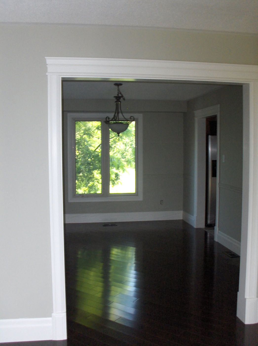 Wide doorway with white casing and header trim over dark hardwood