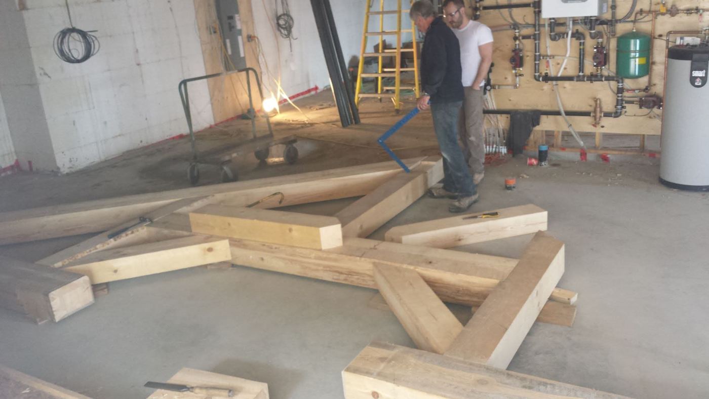 Two carpenters checking a timber truss laid out on a shop floor